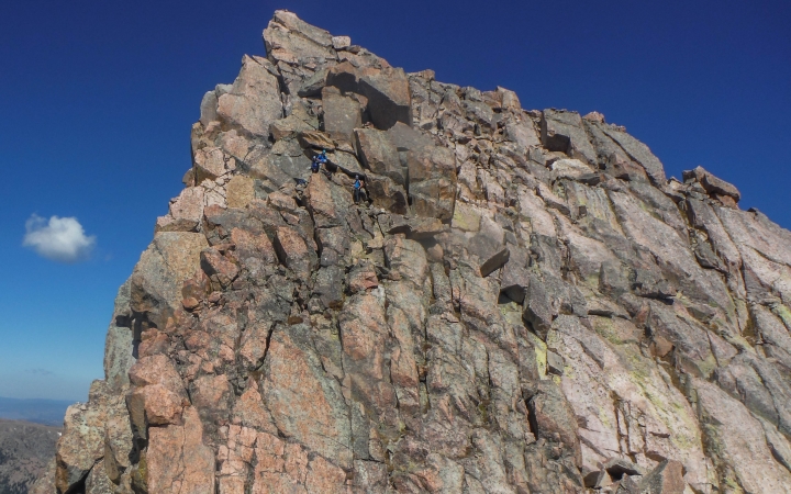 rock climbers make their way up a steep rock wall